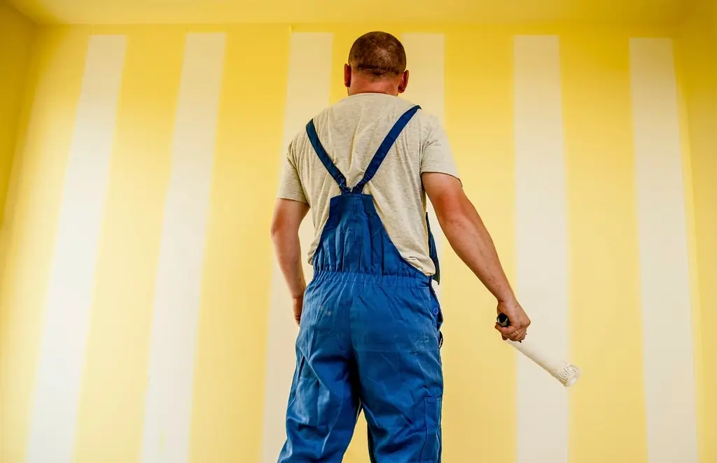 Decorator in overalls rolling fresh paint onto a wall